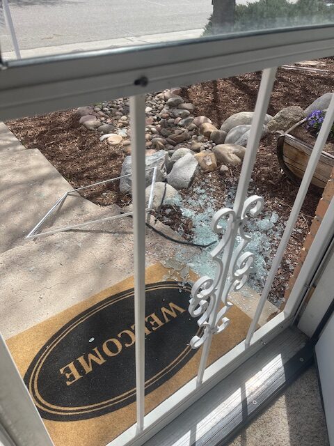 Looking through front screen door to see shattered glass across the step and surrounding landscaping.